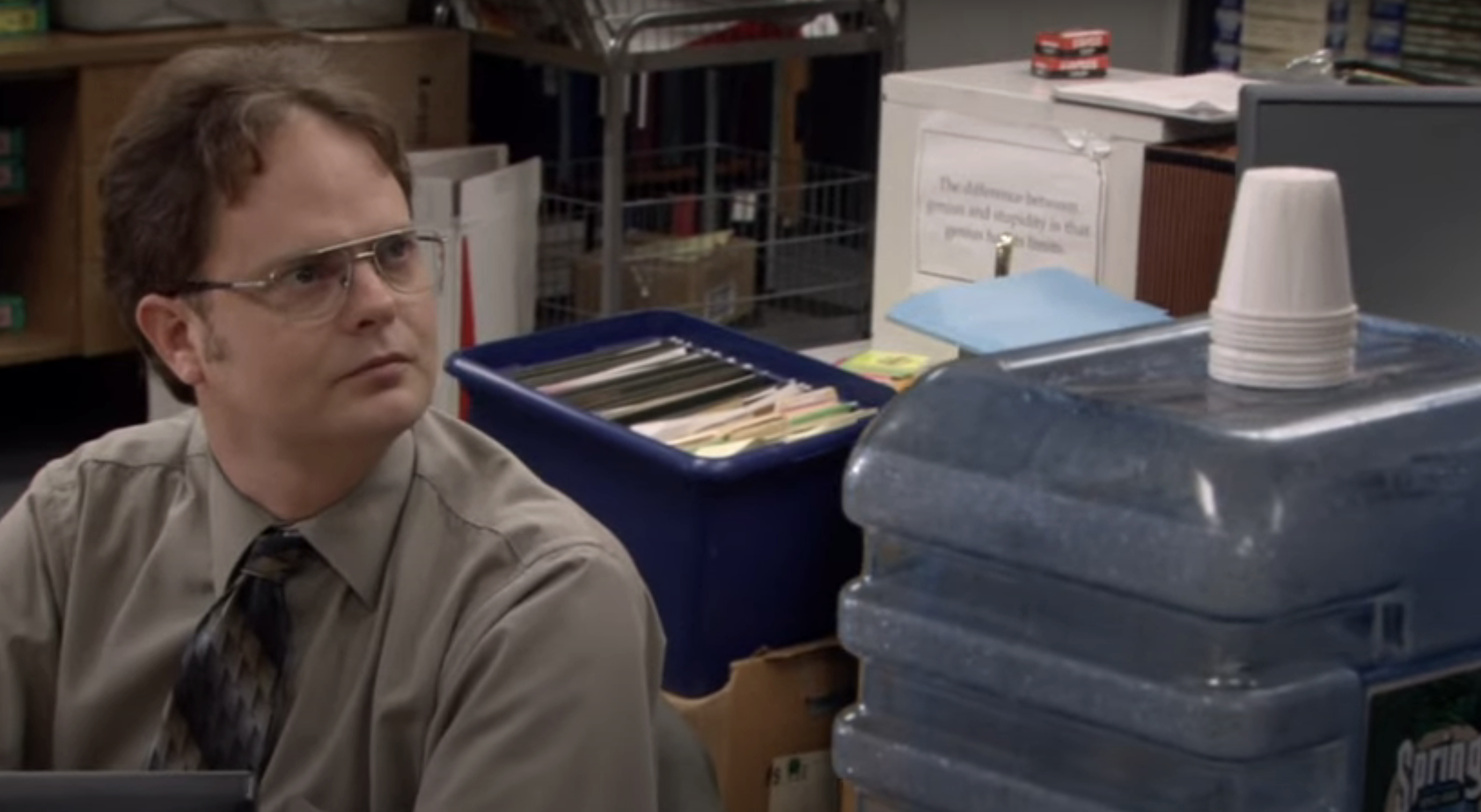 Character Dwight from &quot;The Office&quot; sits at a desk, looking to the side with a serious expression