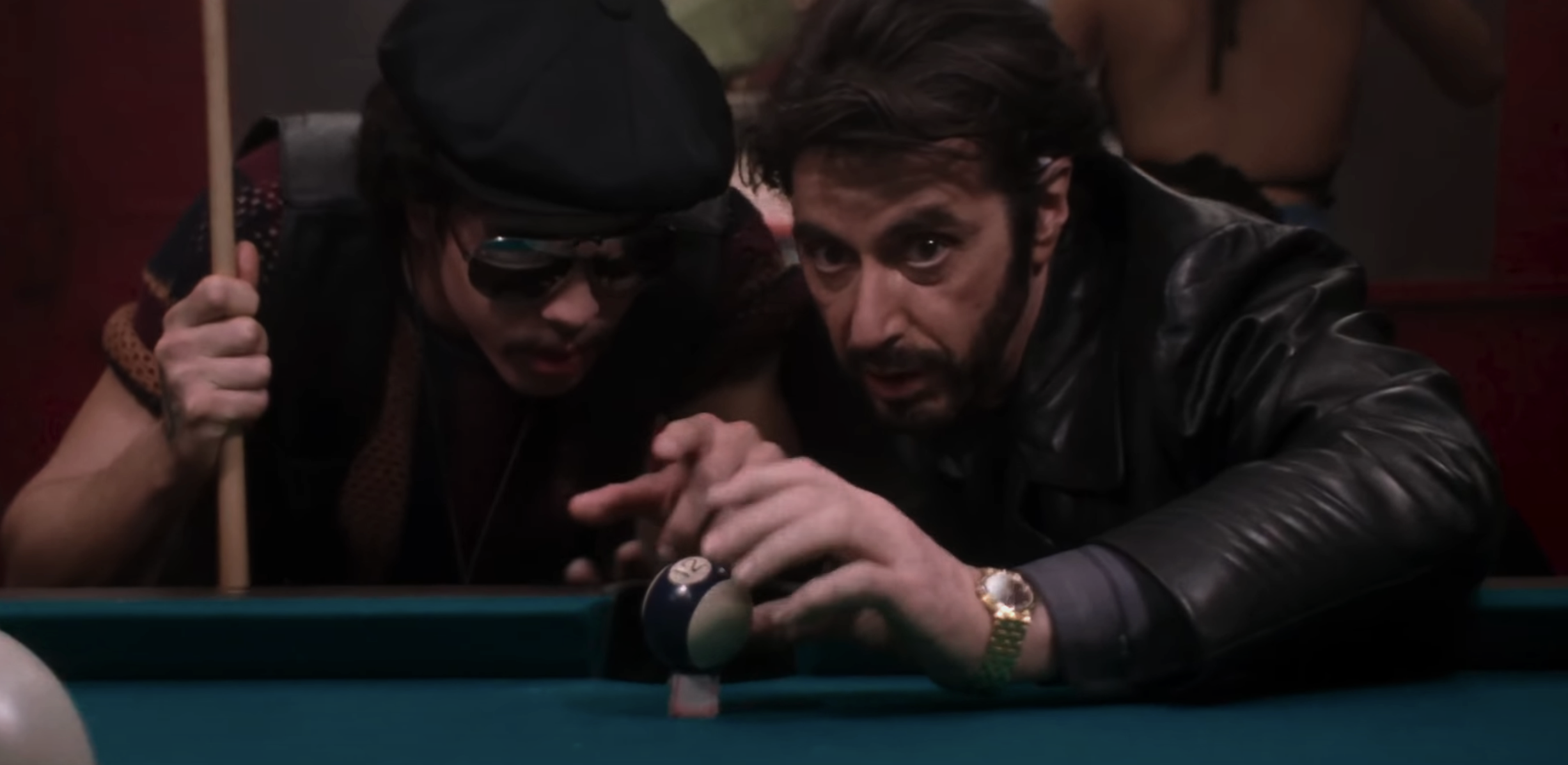 Two men playing pool, one aiming the cue, the other observing closely