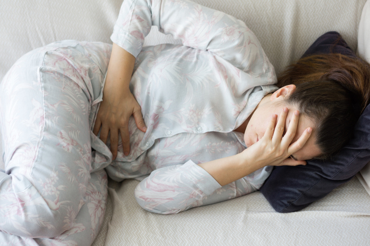 Person lying in bed with hand on forehead, wearing floral pajamas, appears to be unwell or upset