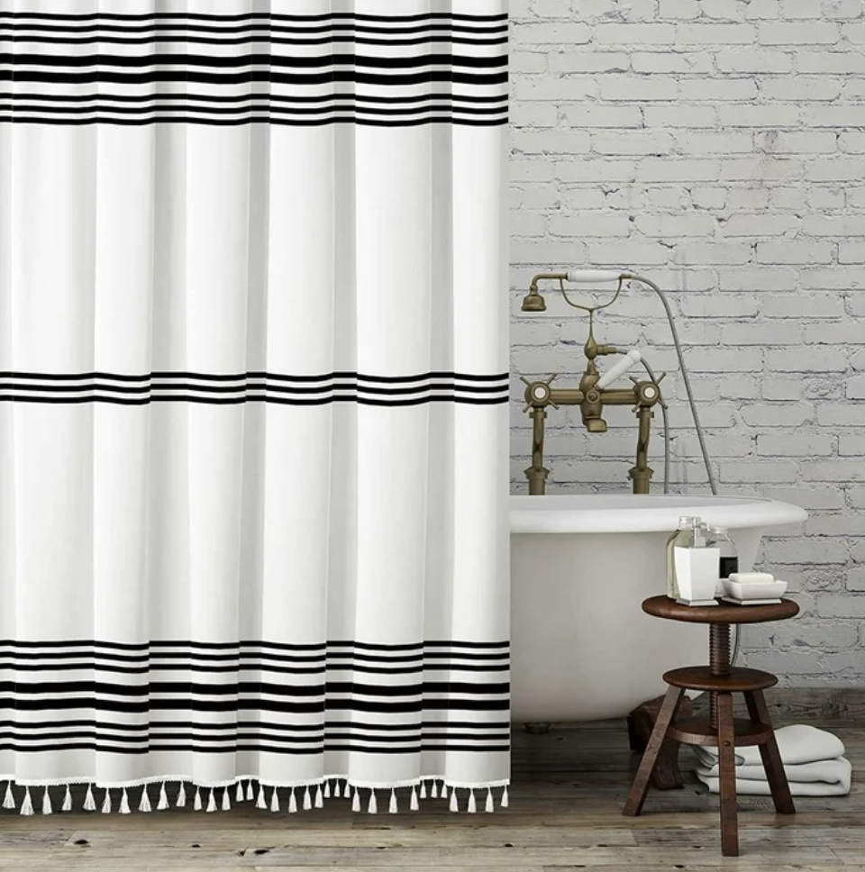 Striped shower curtain with tassel trim in a bathroom with a vintage bathtub and a wooden stool
