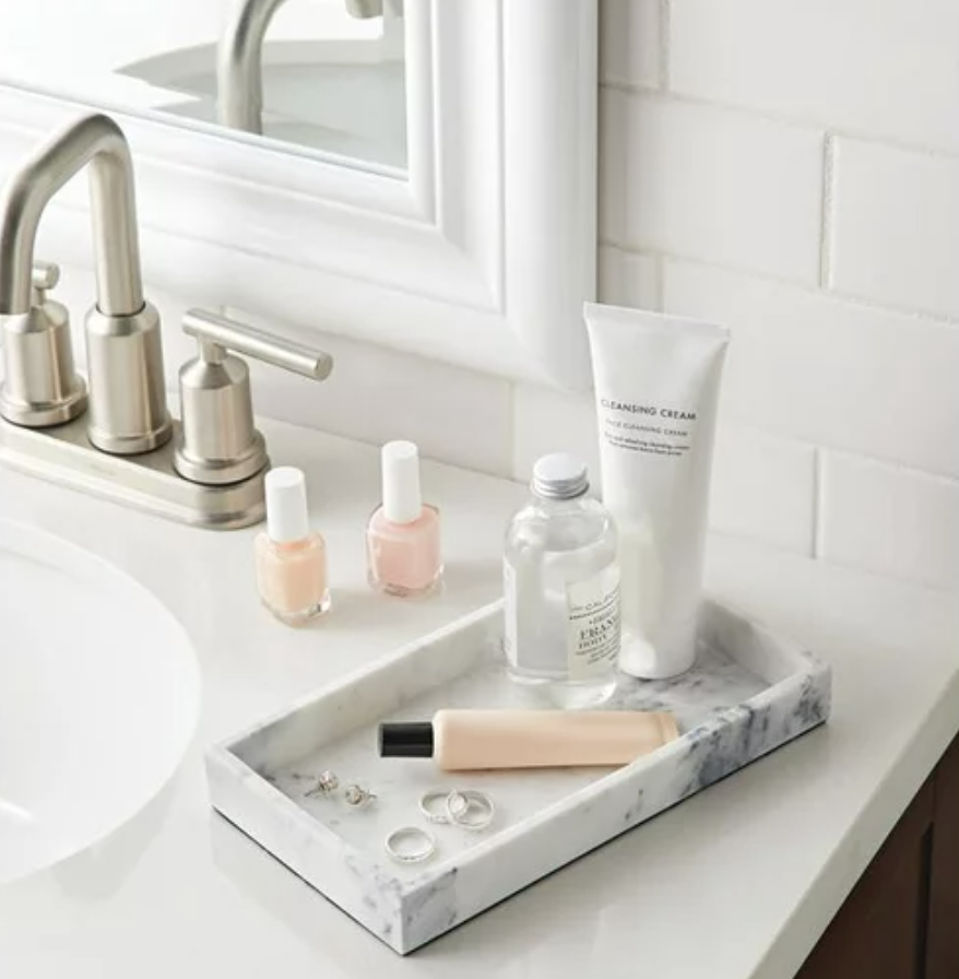 Bathroom countertop with a faux marble tray holding skincare products, nail polish, and accessories
