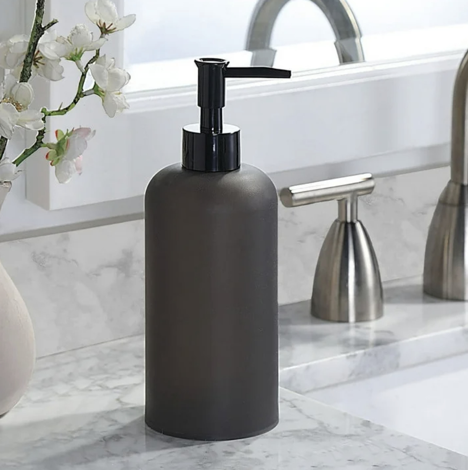 Matte black soap dispenser on a marble countertop beside a sink