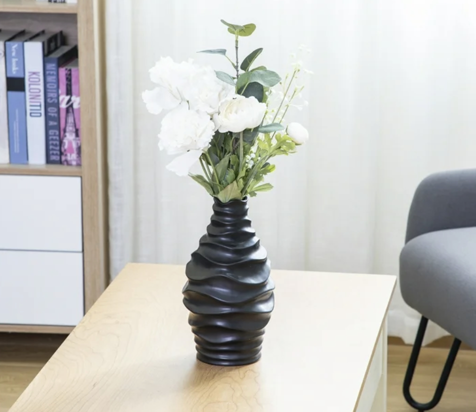 A black twisted vase with white flowers on a wooden table