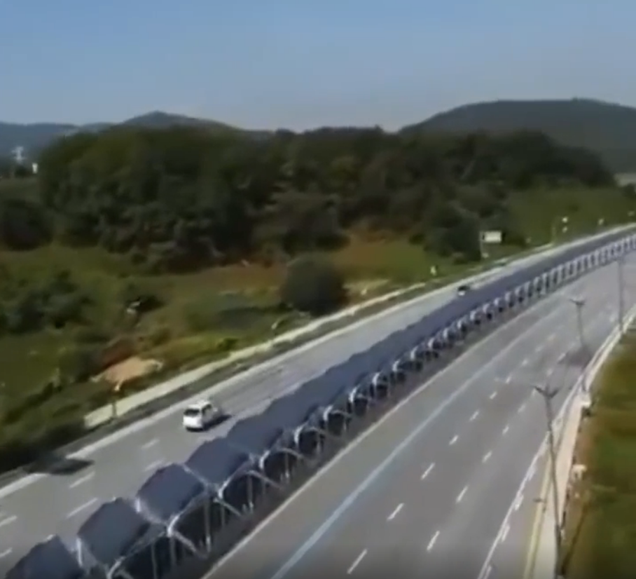 Aerial view of a highway with solar panel canopies covering one side, and a single vehicle on the road
