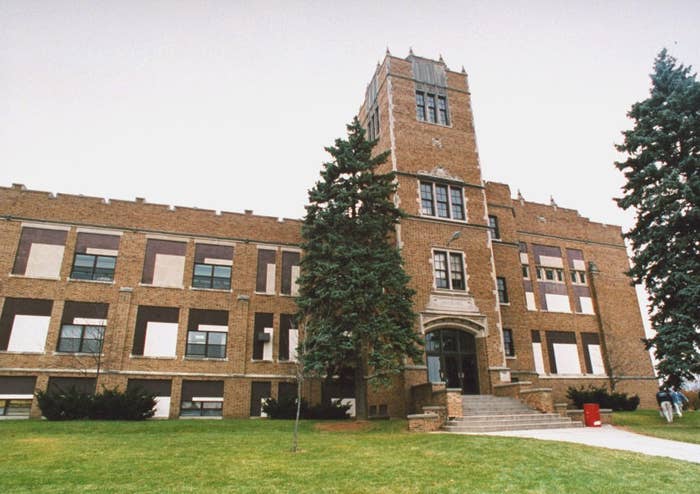 A brick school building with a central tower, grass lawn in front, and trees to the side