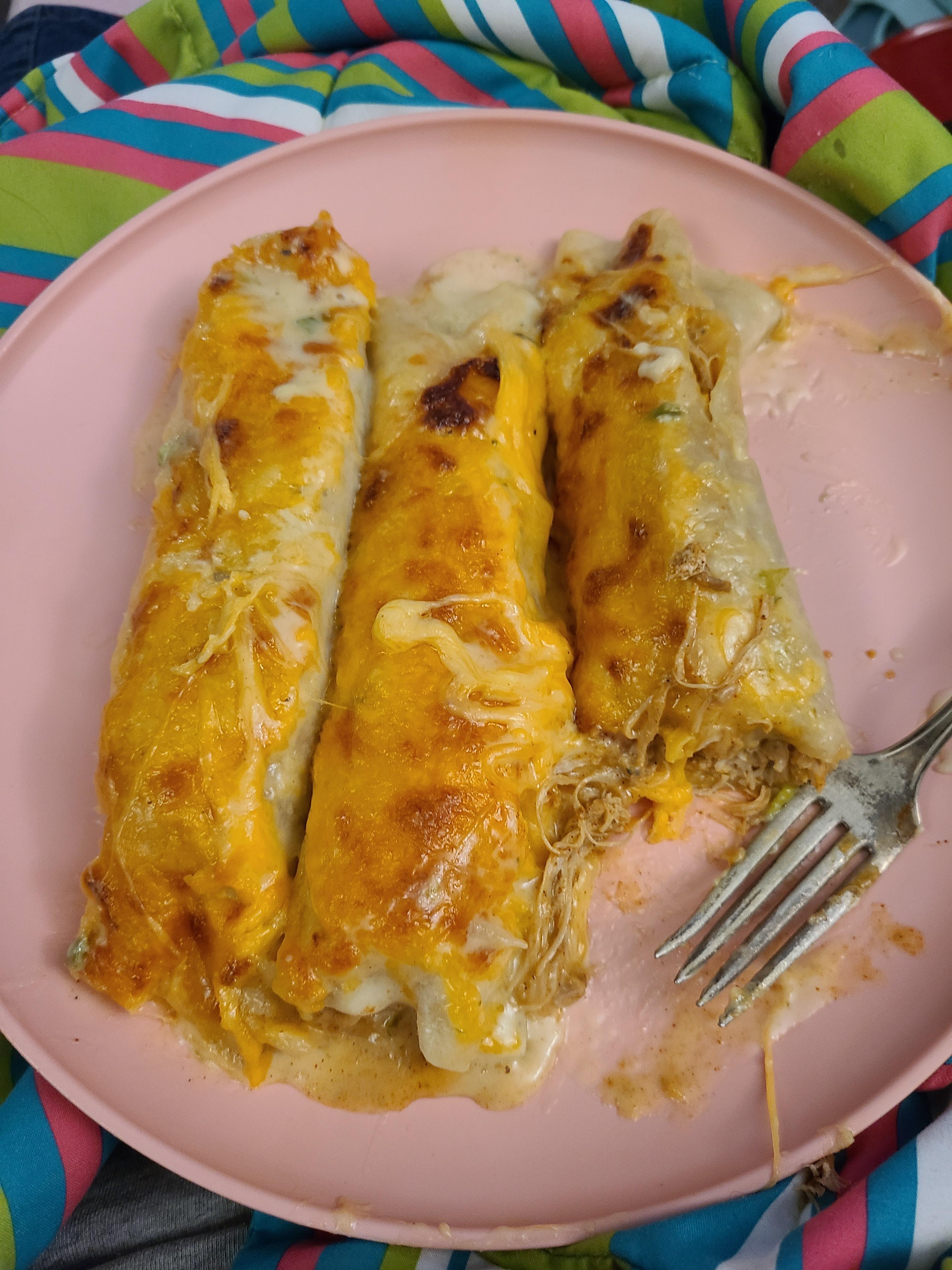 Three cheese enchiladas on a pink plate with a fork