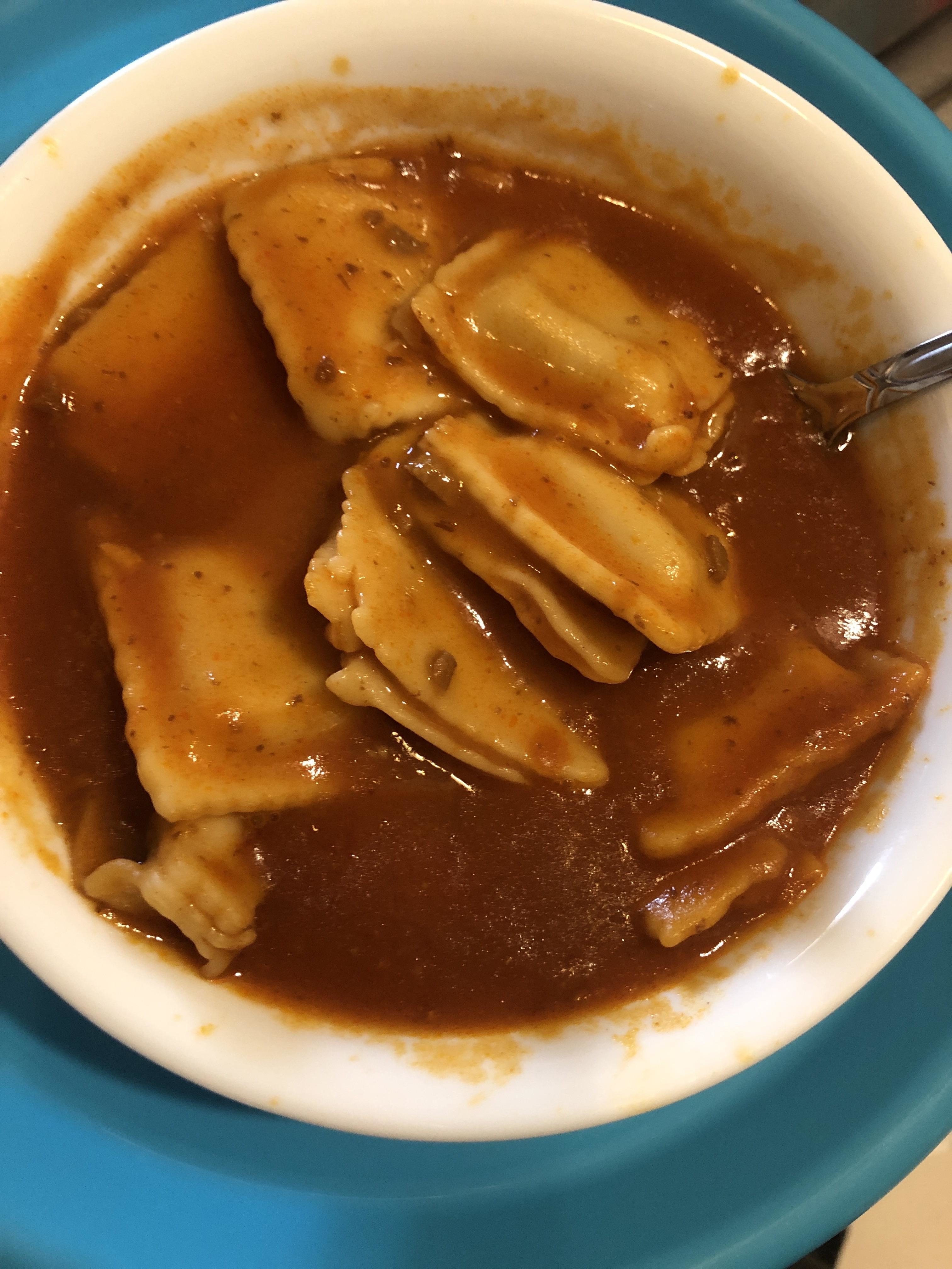 A bowl of ravioli with sauce and a spoon