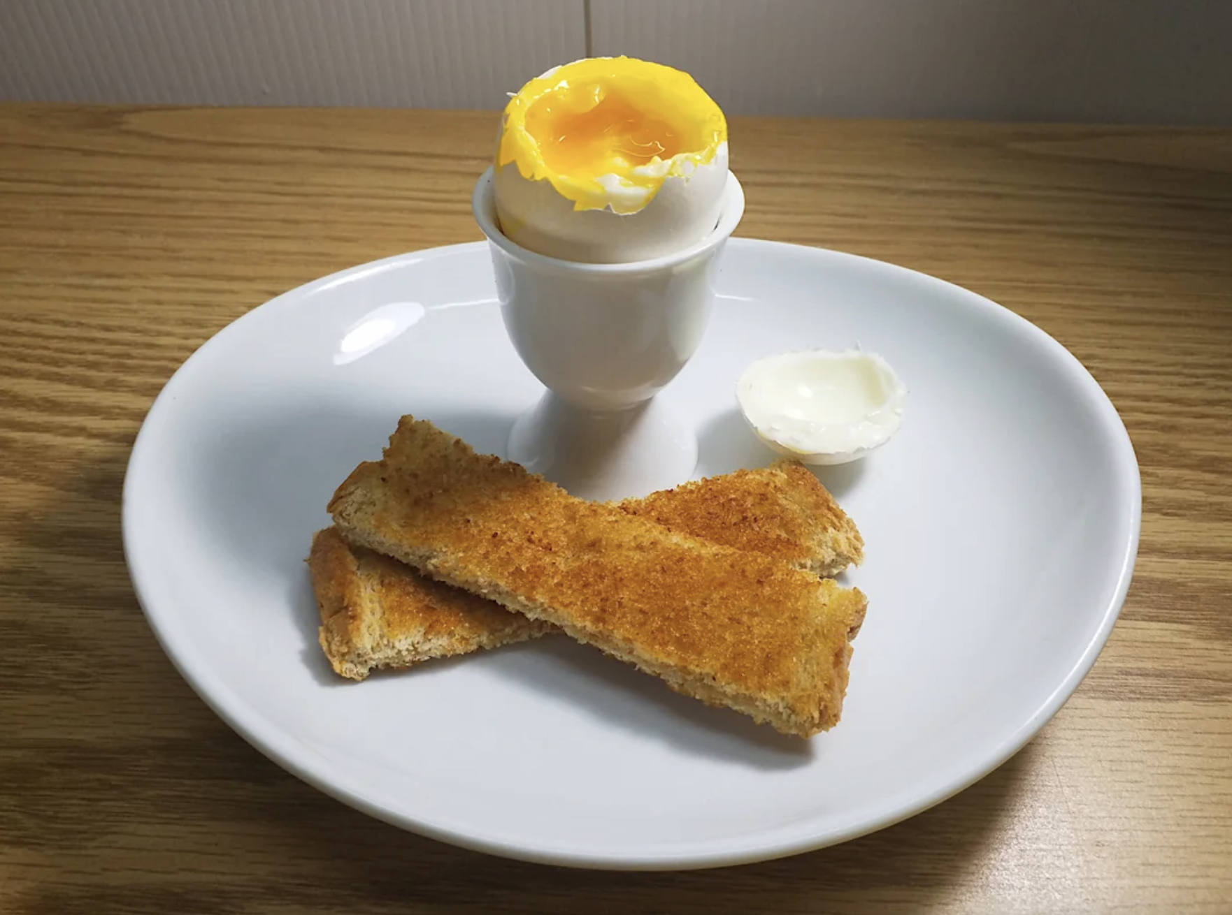 Soft-boiled egg in holder with two toast soldiers and a dollop of butter on a plate