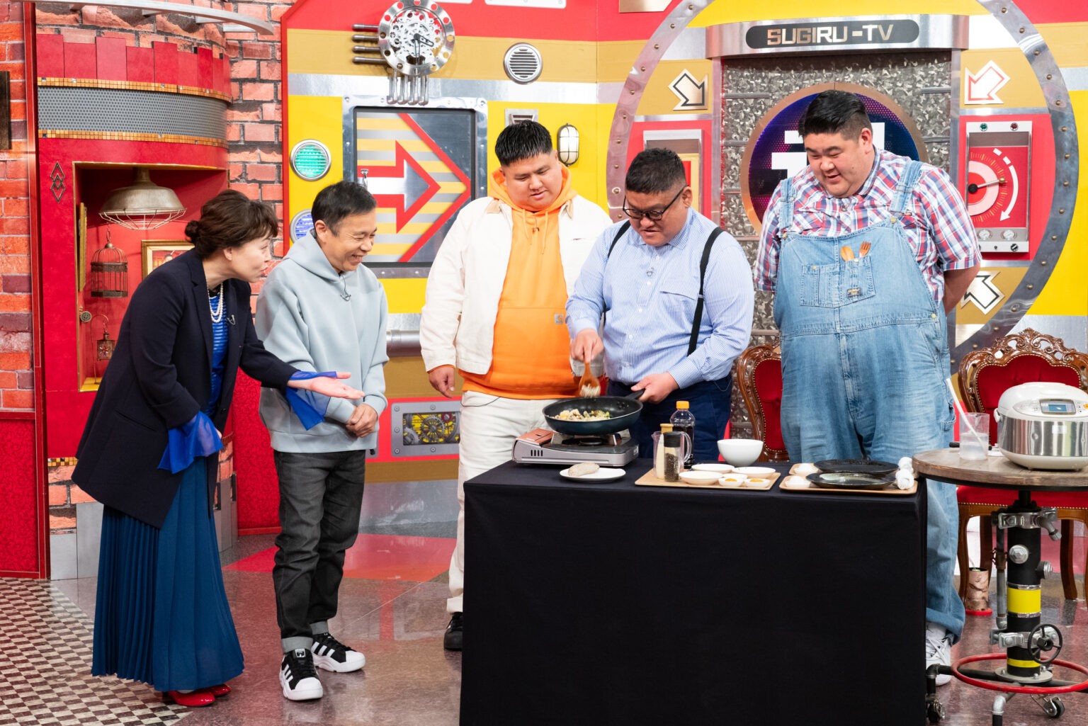 テレビ番組のセットで料理をする人々、注目されている鍋を囲む。具体的な人物の名前は不明です。