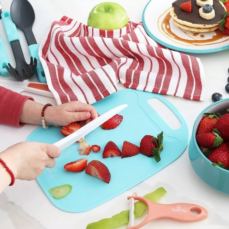 Person slicing strawberries on a light blue cutting board beside a bowl of strawberries and a plated pancake