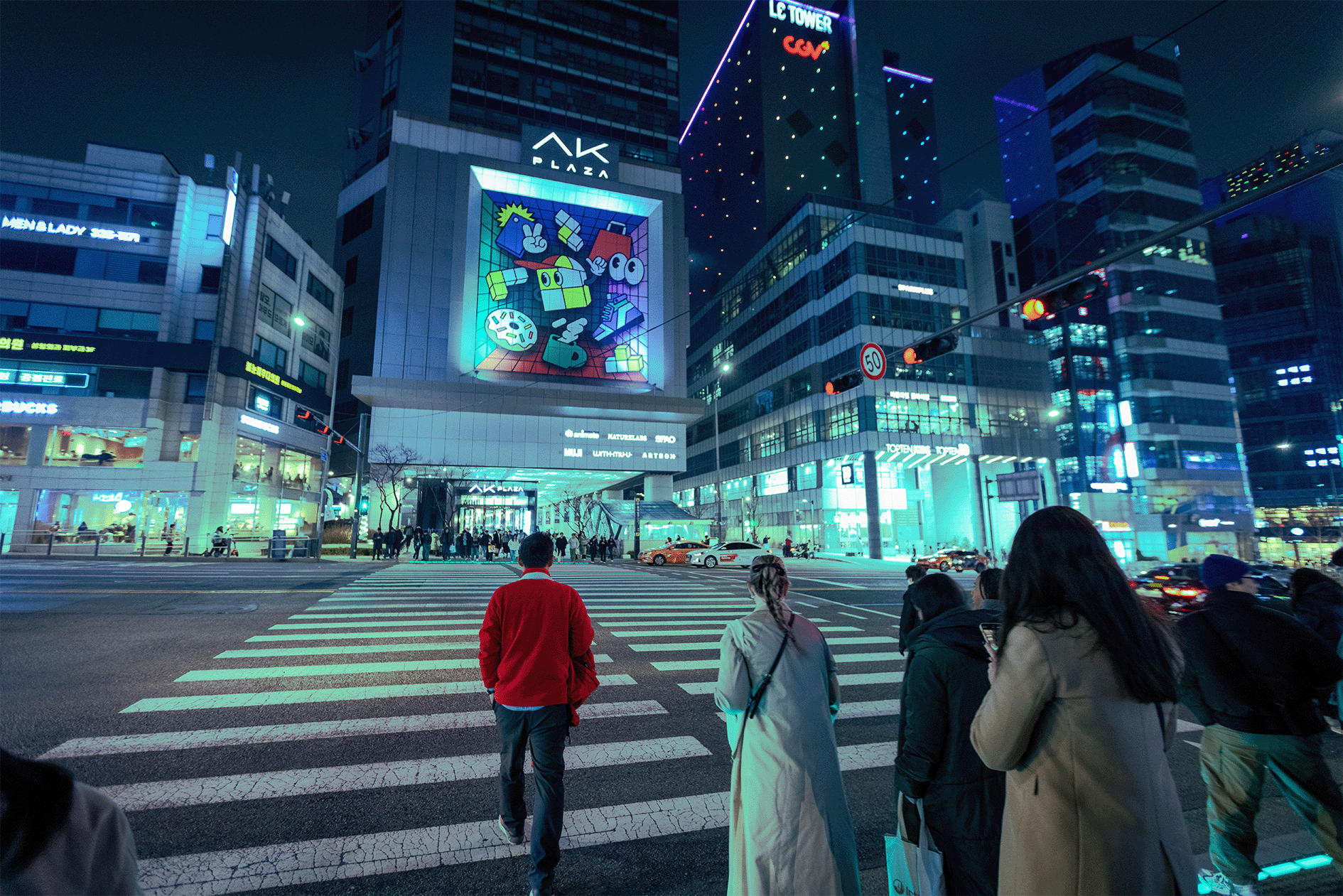 Pedestrians wait to cross at an urban intersection with illuminated billboards at night, no specific persons identified