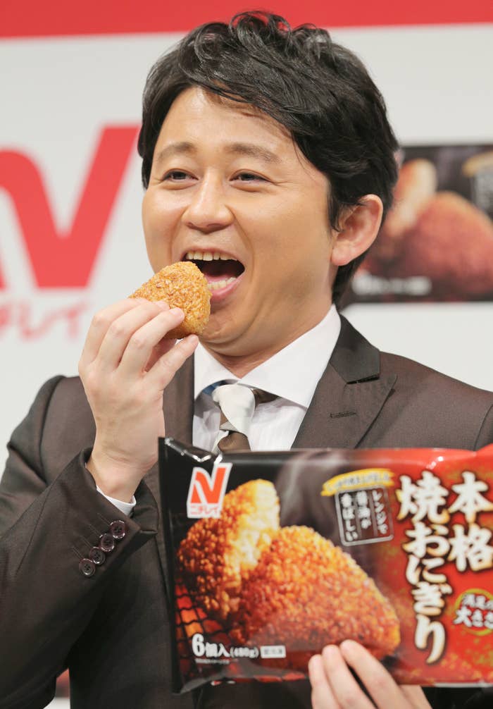 スーツを着た有吉弘行さんが笑顔で手には商品のパッケージを持っています。