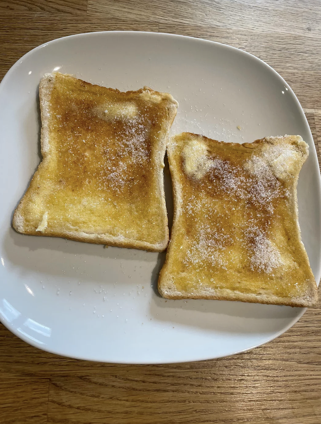Two slices of toast with butter and sugar on a plate