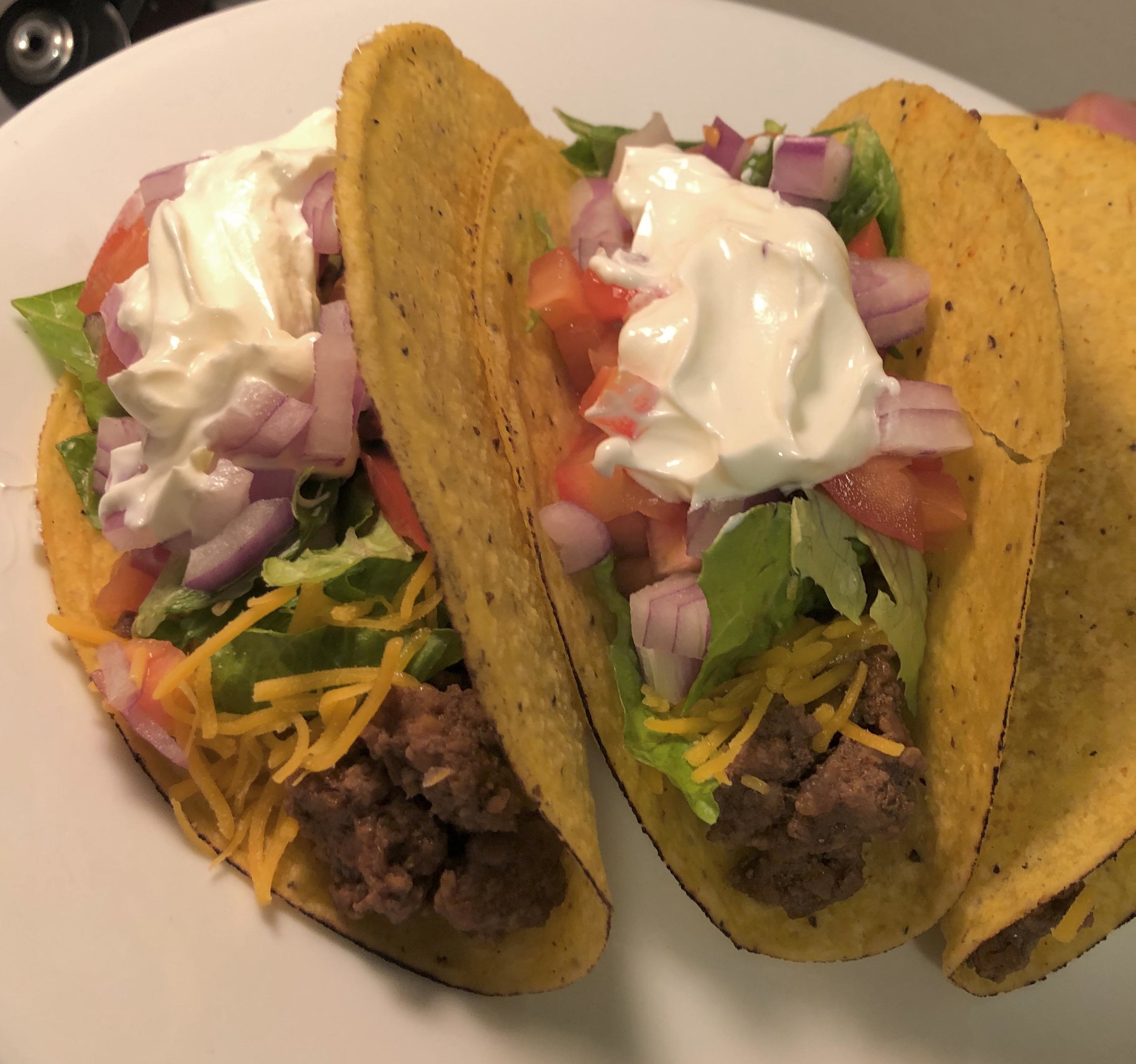 Two tacos with beef, cheese, lettuce, tomato, onions, and sour cream
