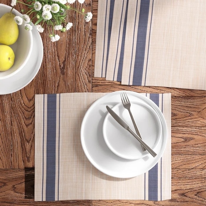 White dinnerware set on a striped placemat with a bowl of lemons and flowers nearby, suggesting a home decor theme
