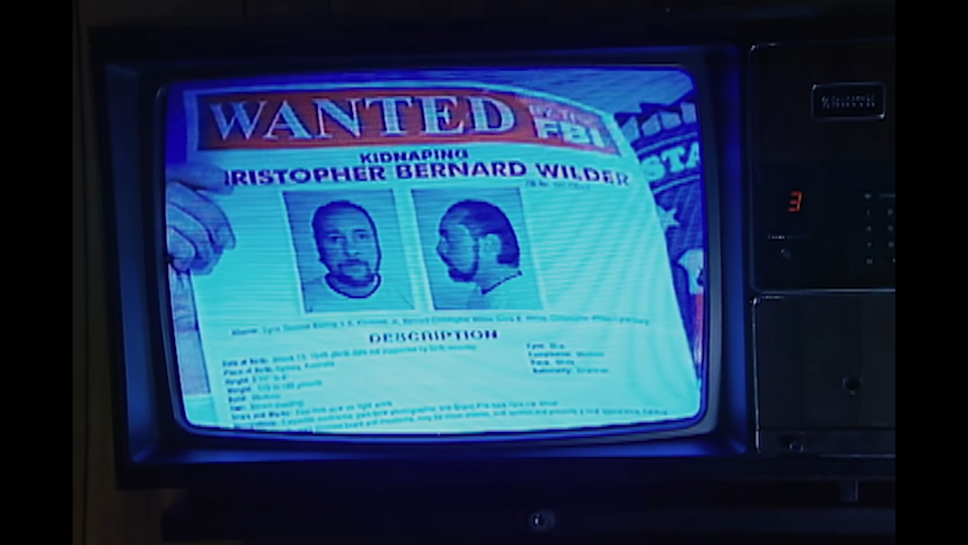 Wanted poster on a TV screen showing photographs and information for Christopher Bernard Wilder