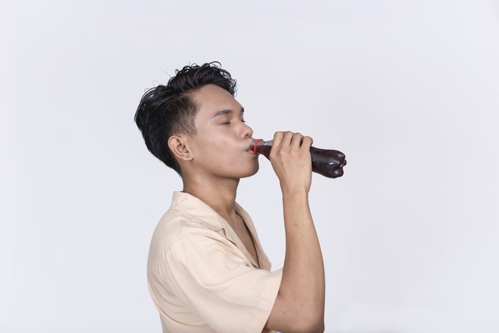 Person drinking from a bottle against a neutral background