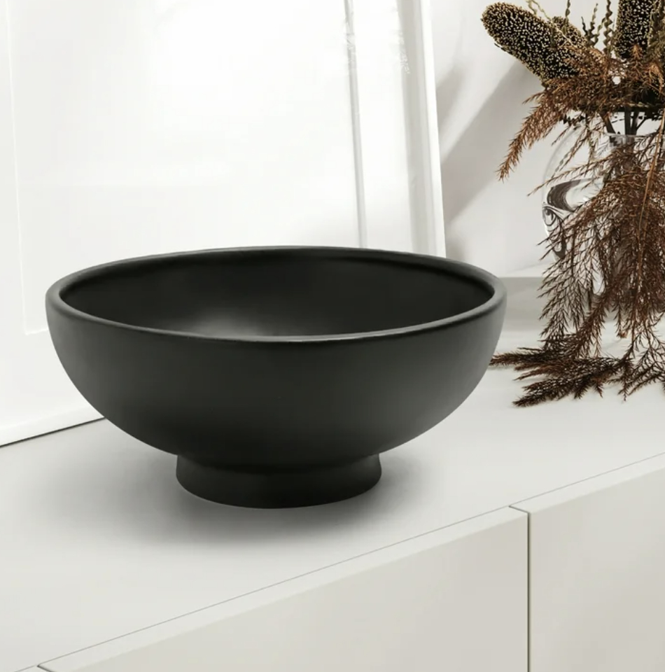 Black modern-style decorative bowl on a white surface near dried plants