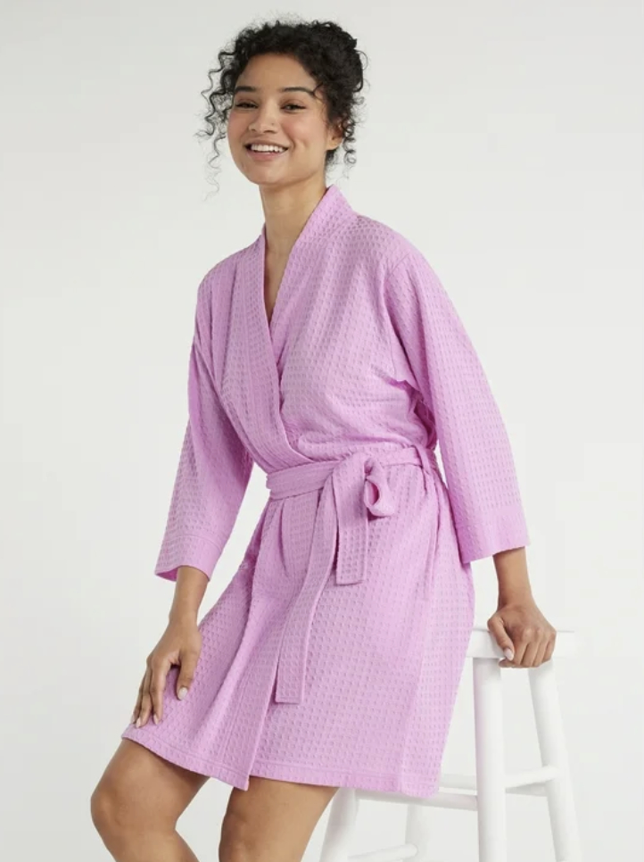 Model smiling, wearing a textured knee-length robe with a tie waist, seated on a stool