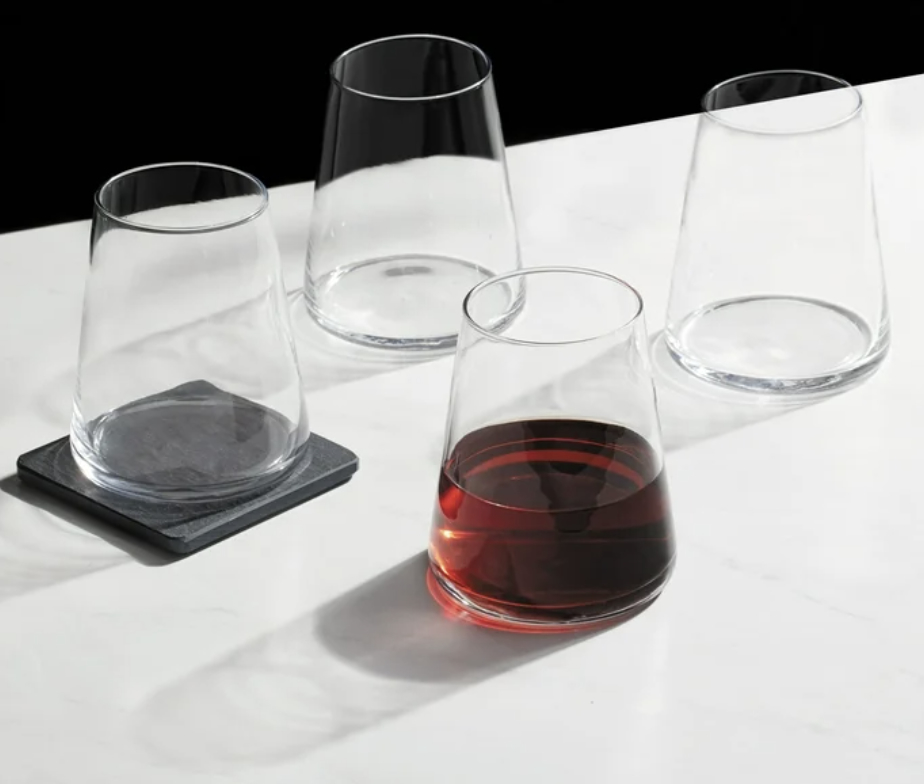 Set of four stemless wine glasses, one filled with red wine, on square slate coasters