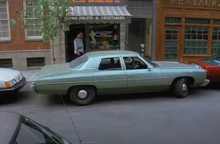 1970s style sedan car on a city street with storefronts and a person in the background