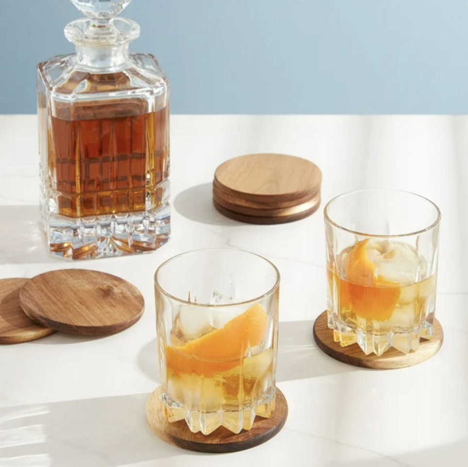 Two whiskey glasses with ice and slices of orange on wooden coasters