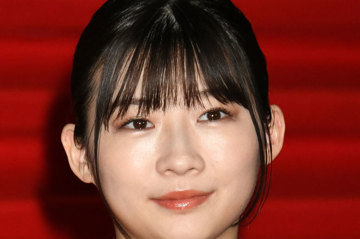 黒いドレスを着た女性が、赤い背景の前でカメラを見ています。