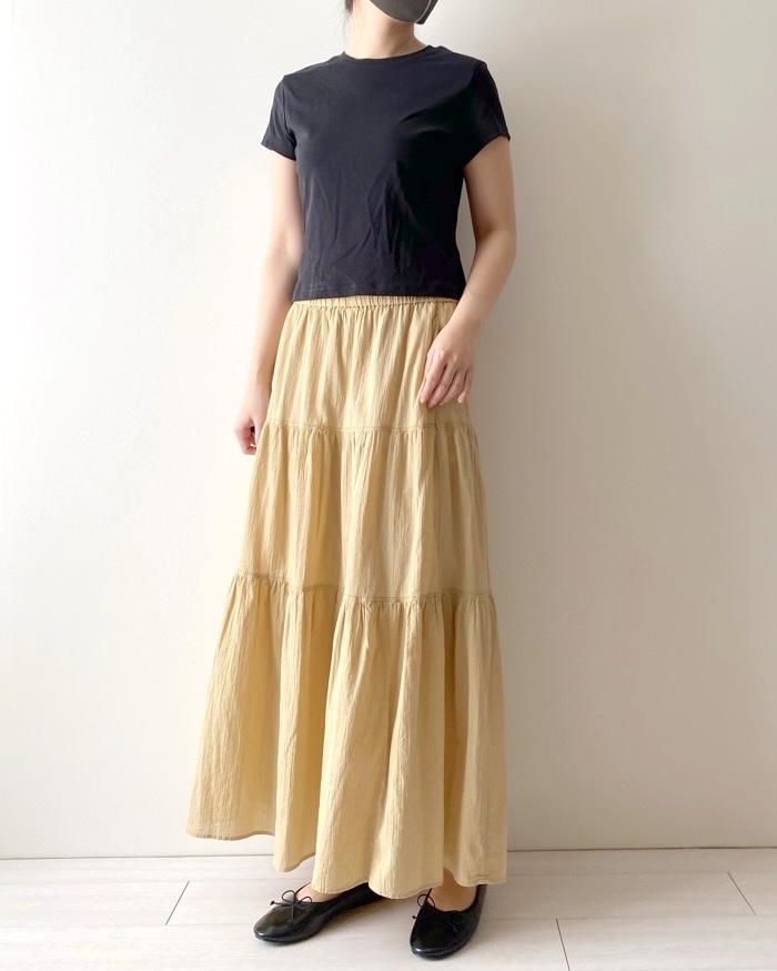 Person standing wearing a black T-shirt paired with a tiered maxi skirt and black flats. Identity not visible