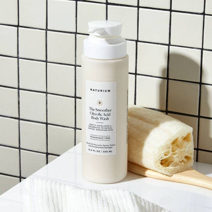 Bottle of Naturium Glycolic Acid Body Wash on counter next to a sponge, for a shopping guide