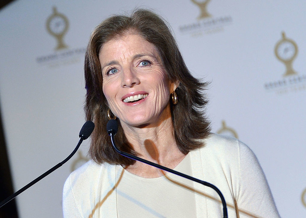 Caroline Kennedy at podium smiling in a formal event, wearing a simple long-sleeved top