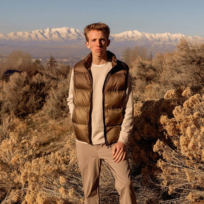 Man in vest and sweater standing in a field with mountains in the background, for a sports-related article