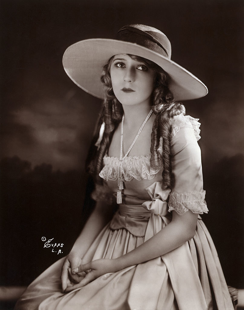 Vintage portrait of Mary with braided hair, wearing a large-brimmed hat and a dress with ruffled sleeves
