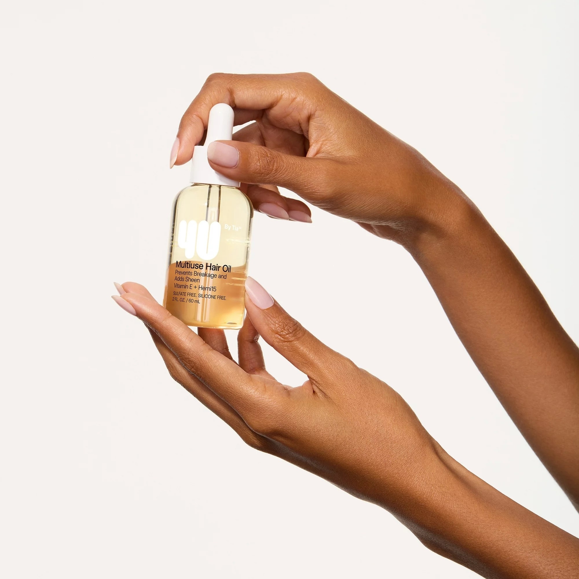 Hands holding a bottle of multiuse hair oil against a neutral background, suitable for article on beauty shopping
