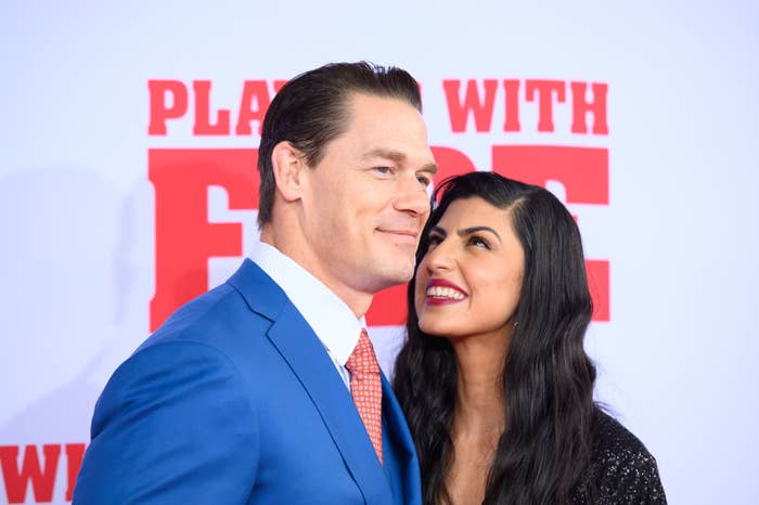 John Cena in a suit and Shay Shariatzadeh in a dress smiling on the red carpet