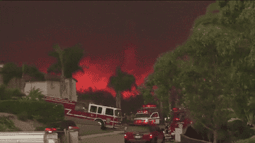 Firefighters and fire engines at night with a large wildfire visible in the background