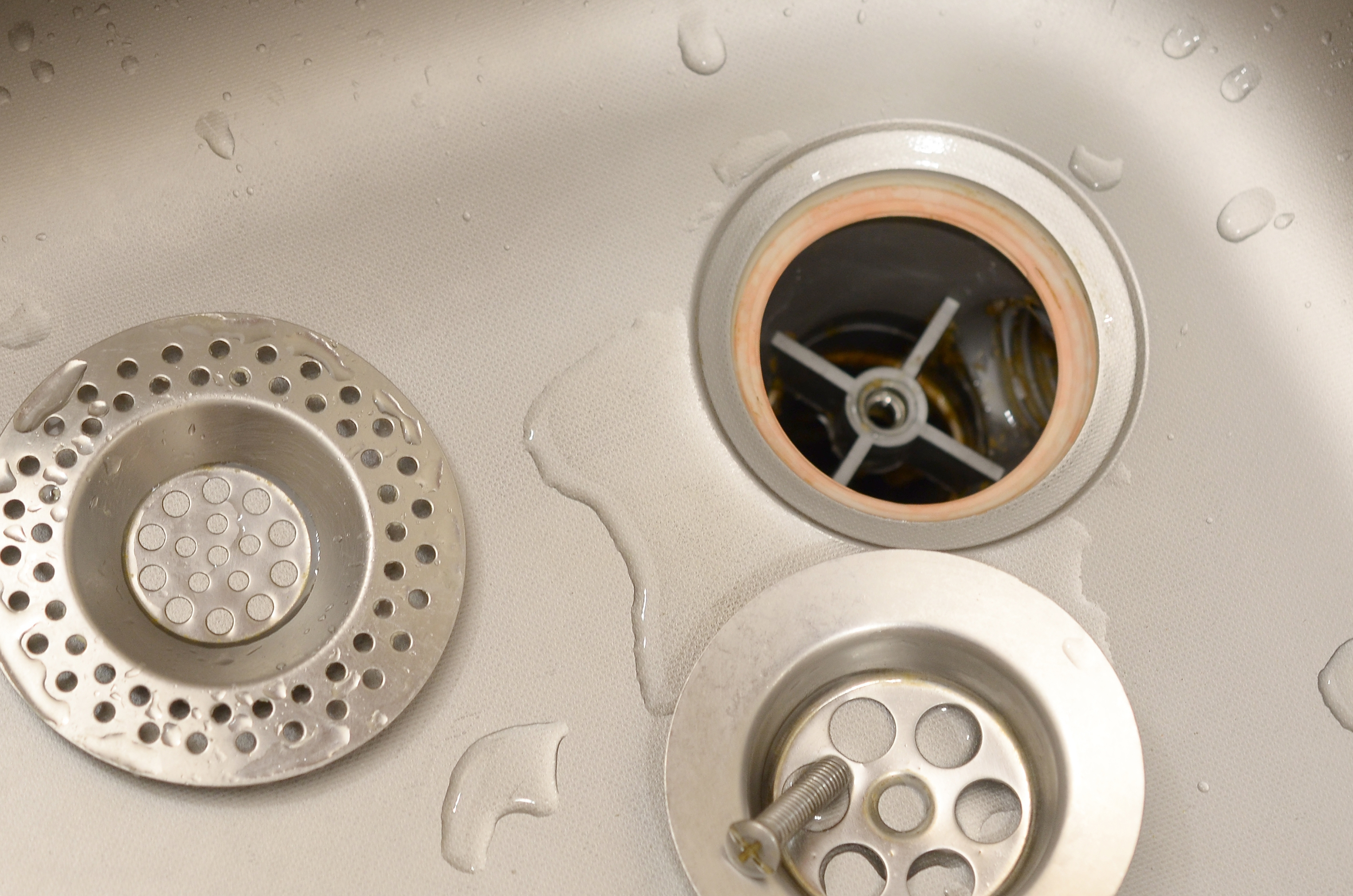 Close-up of a kitchen sink with visible water droplets, focusing on the drain and garbage disposal