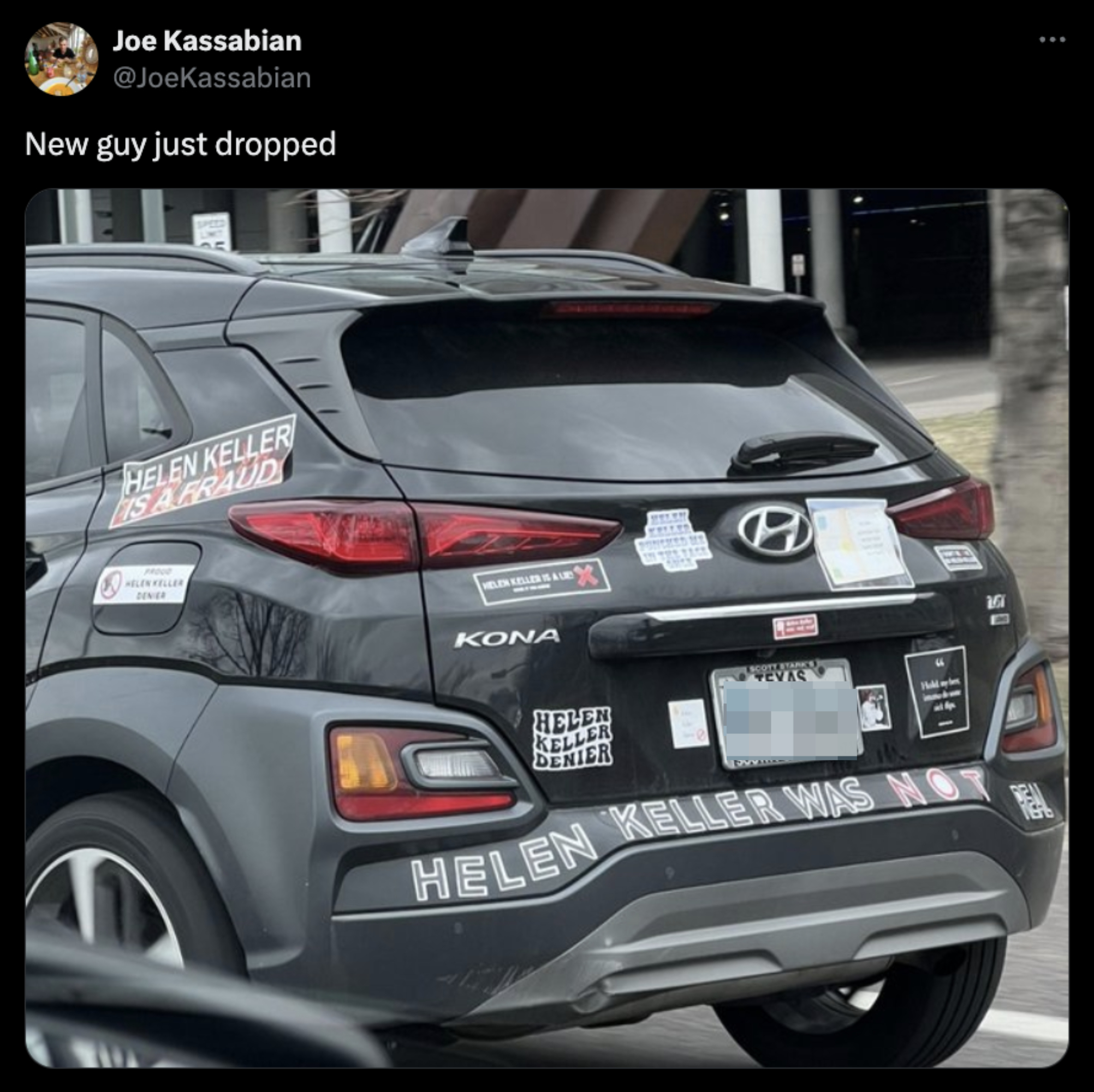 Car with multiple &#x27;Helen Keller is a fraud&#x27; stickers, internet meme-centric decorations, in motion on the street