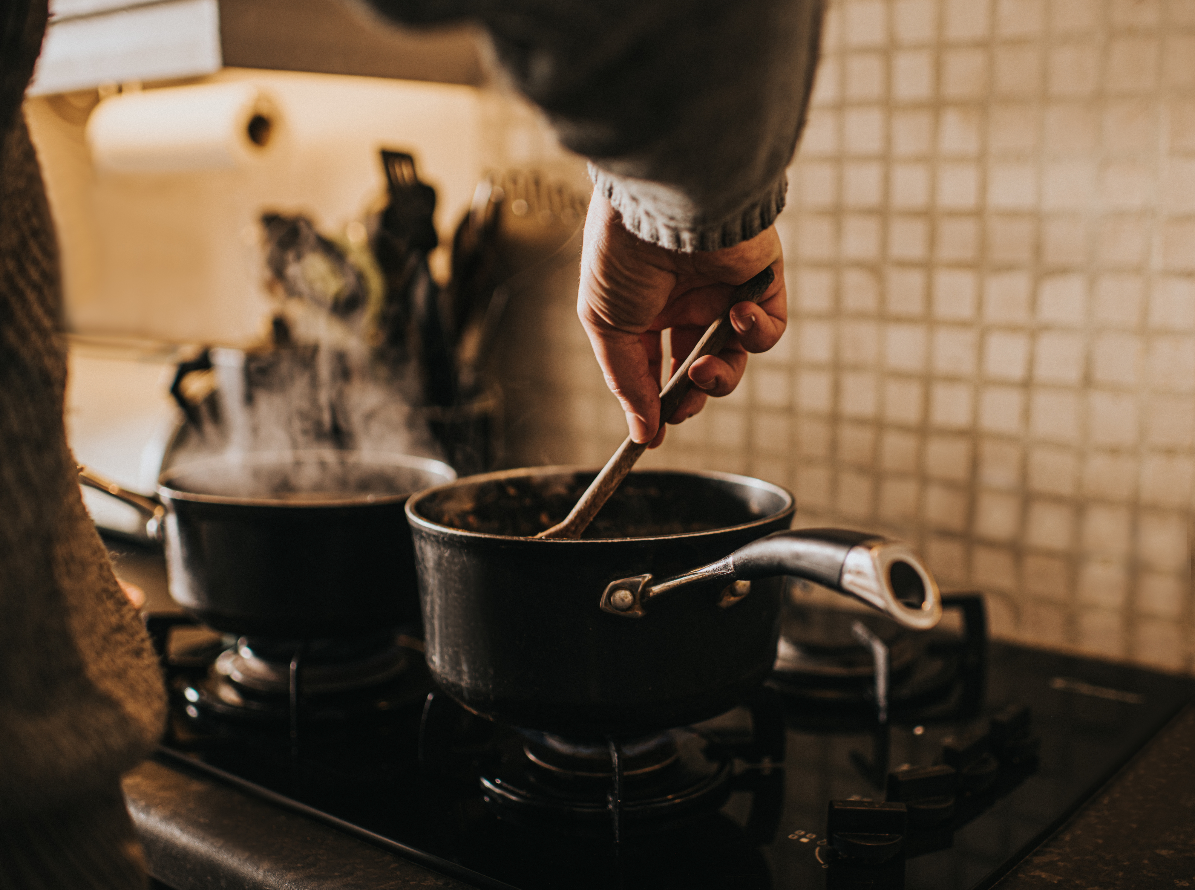 Person cooking, stirring a pot on the stove with steam rising