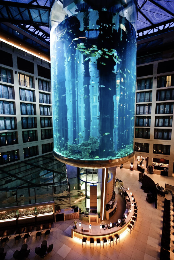 Giant cylindrical aquarium spanning several floors in a building&#x27;s atrium, surrounded by balconies and seating areas