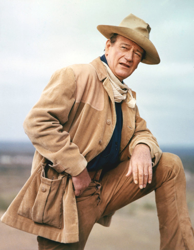 John Wayne in a western outfit with a hat and jacket, posing with a hand on his hip