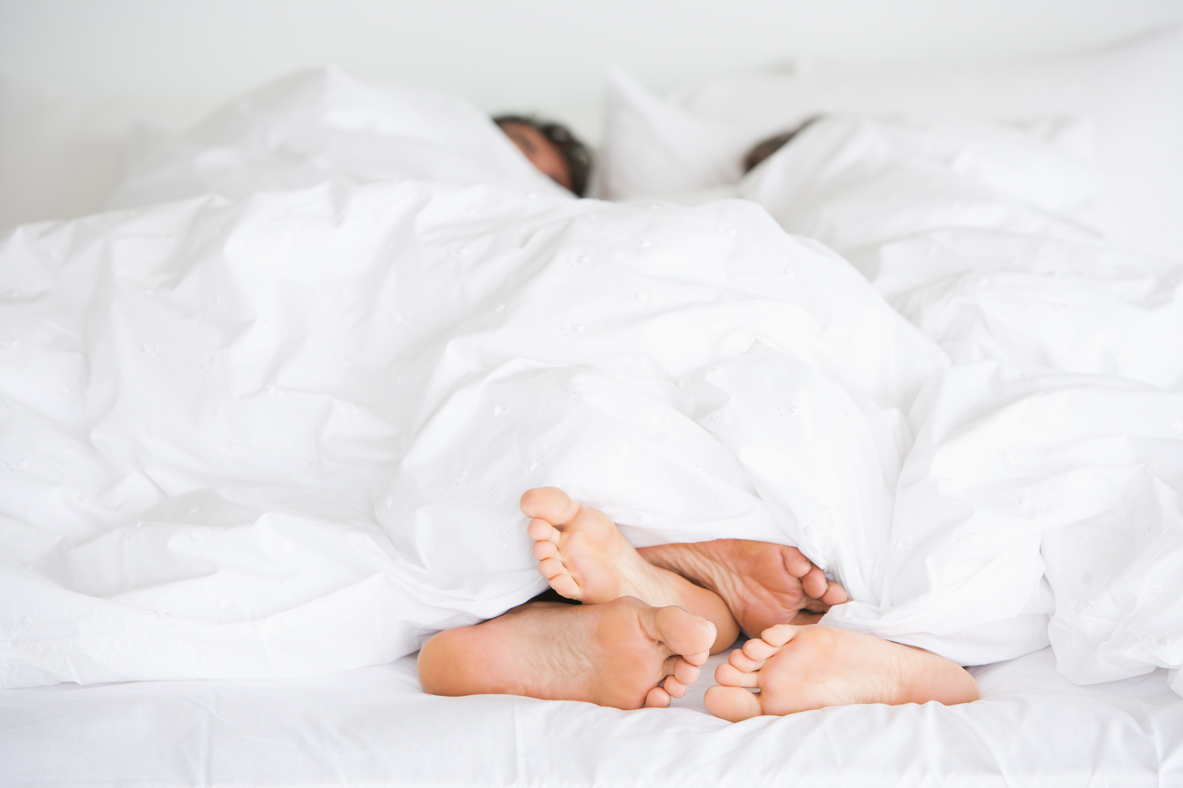 Two people&#x27;s feet sticking out from under a white duvet, suggesting intimacy