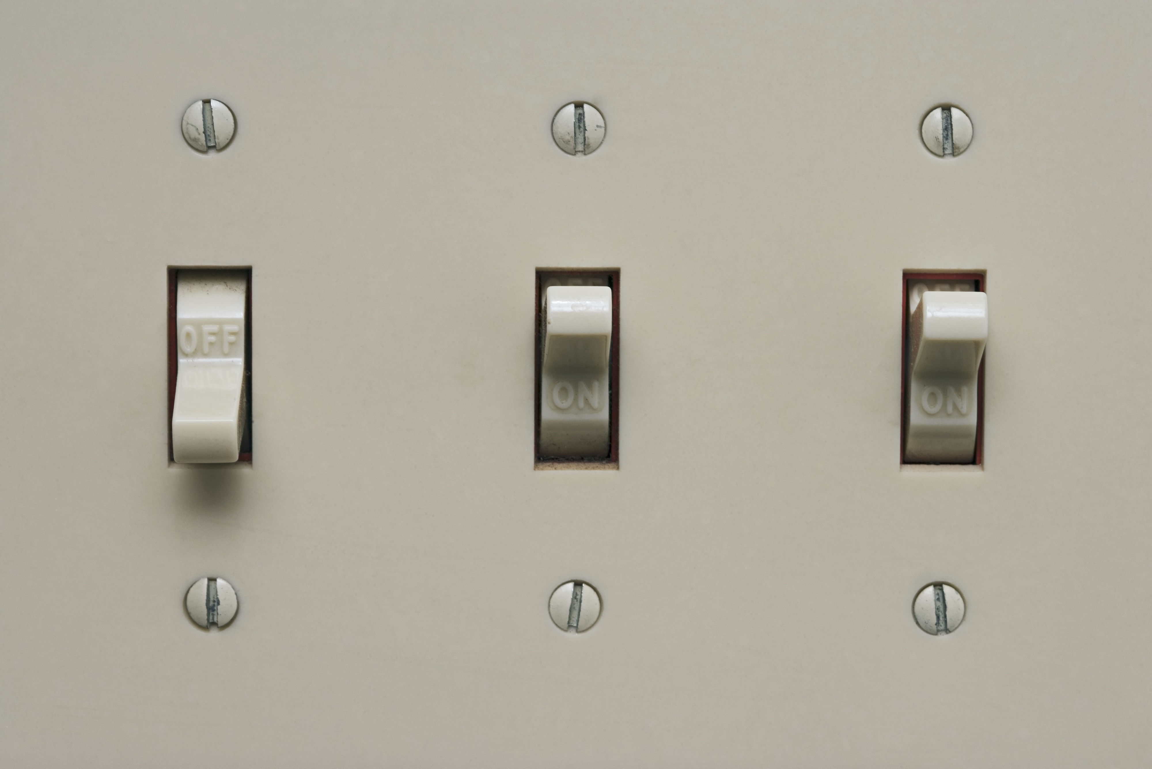 Three light switches on a wall, with the middle switch in the &#x27;ON&#x27; position and the others &#x27;OFF&#x27;
