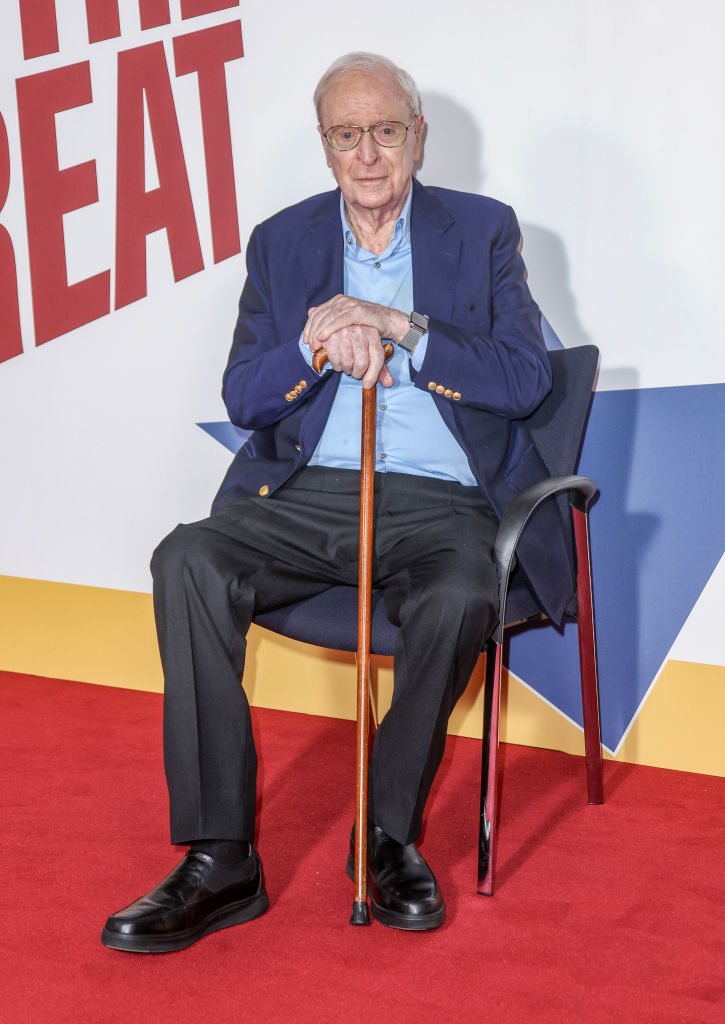 Michael in suit and glasses sitting with a cane against a graphic background