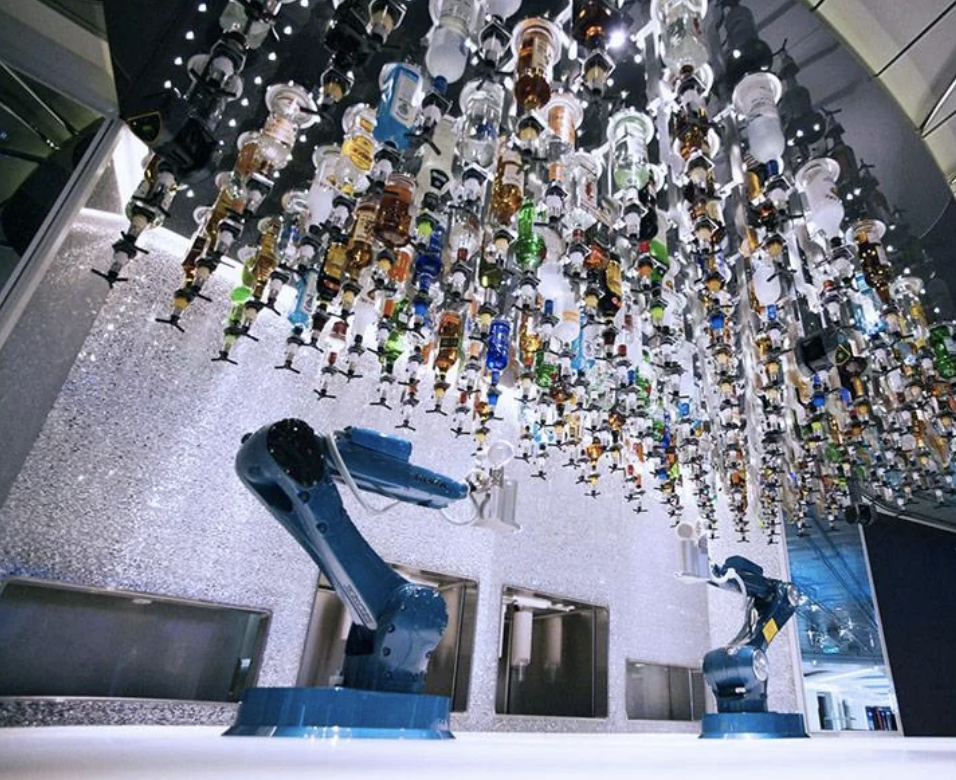 A robotic arm beneath a ceiling-mounted array of various hanging bottles in a modern installation