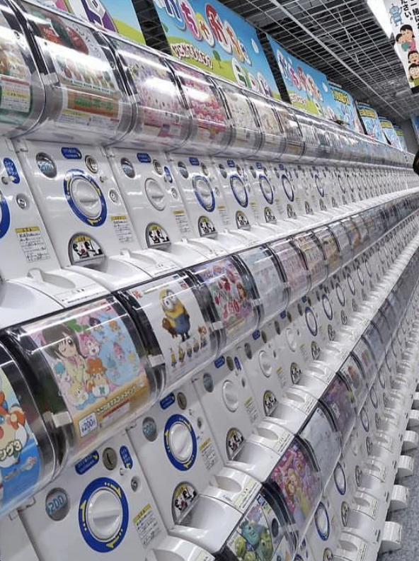 A row of Japanese gachapon toy capsule vending machines with various cartoon characters