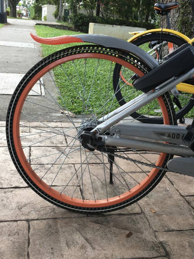 Parked bike with a unique orange-tire design on a paved path with grass and trees in the background