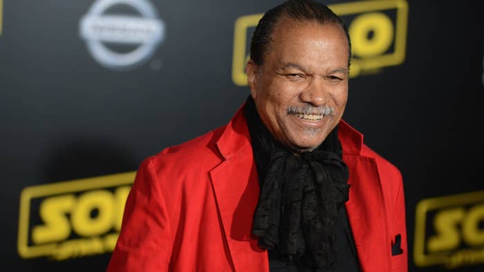 Billy Dee Williams in a red jacket and black scarf at an event