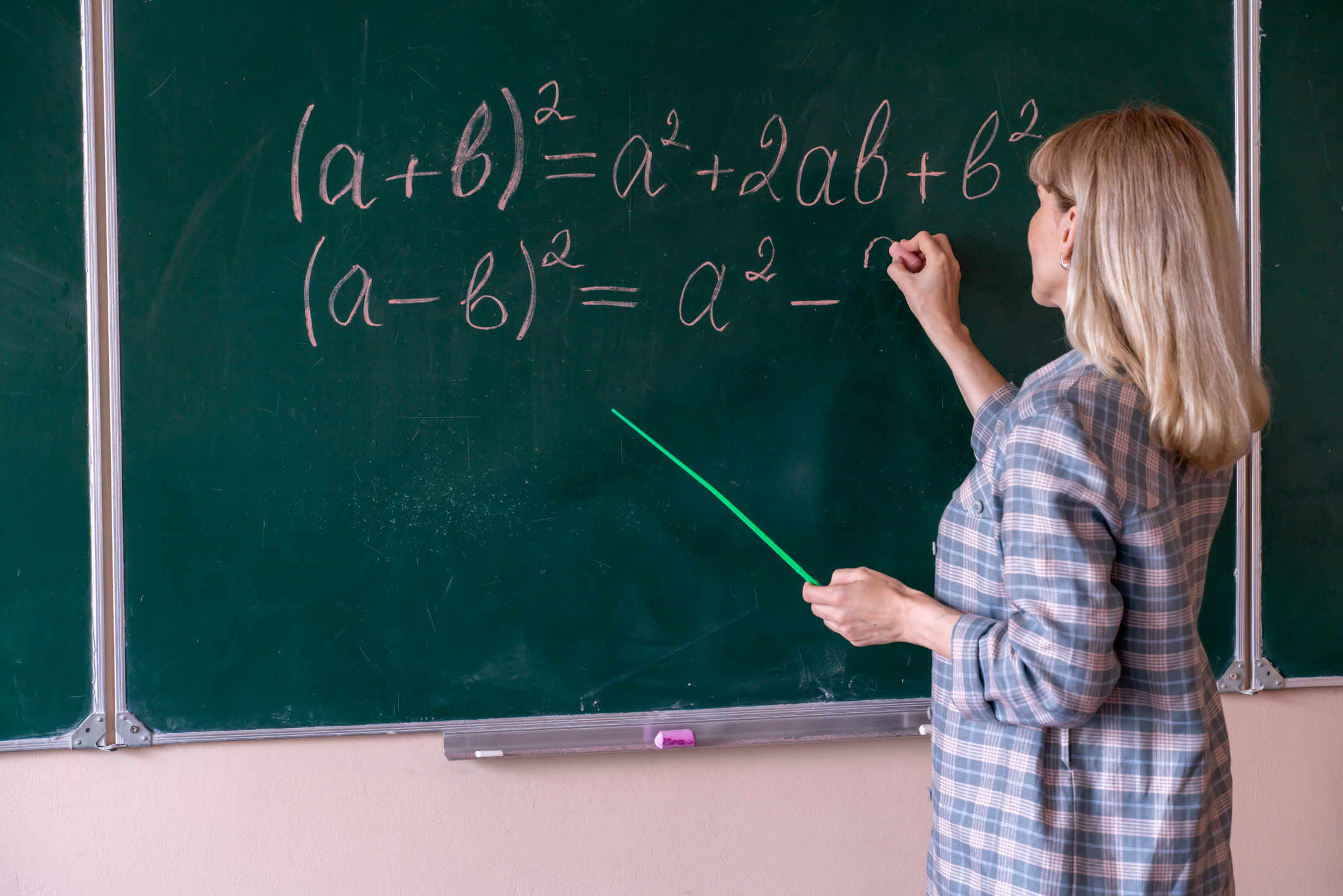 Woman teaching algebra on a chalkboard, pointing with a rod