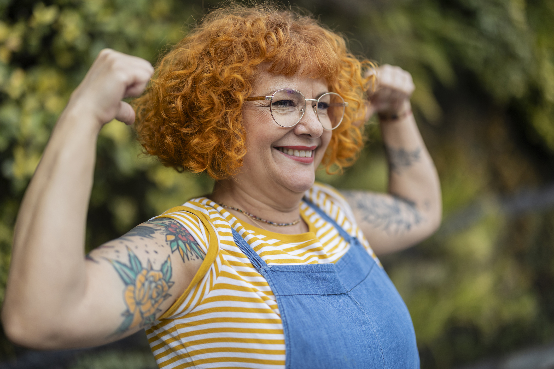 A woman in overalls flexing her arms and smiling