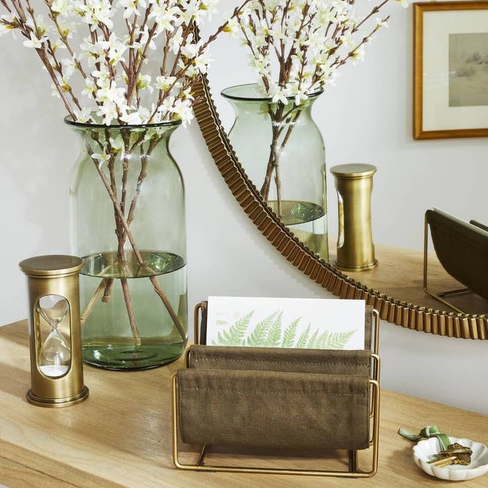 Home decor items on a table, including a vase with branches, hourglass, candle holder, and a leaf-design napkin in a holder
